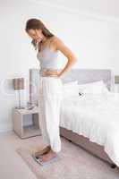 Fit young woman standing on scale in bedroom