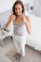 Wwoman on scale gesturing thumbs ups in bedroom