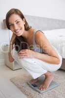 Fit young woman crouching on scale in bedroom