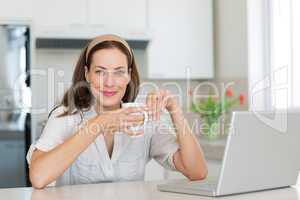 Smiling woman with coffee cup and laptop in kitchen