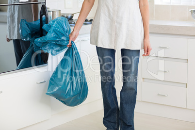Low section of woman carrying garbage bag in kitchen