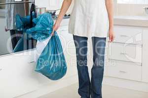 Low section of woman carrying garbage bag in kitchen