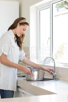 Side view of woman with vessel at washbasin in kitchen