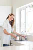 Smiling woman with vessel at washbasin in kitchen