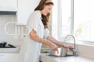 Side view of woman with vessel at washbasin in kitchen