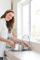 Smiling woman with vessel at washbasin in kitchen