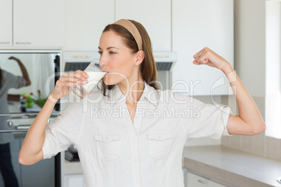 Woman flexing muscles while drinking milk in kitchen