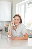 Smiling woman with coffee cup using landline phone in kitchen