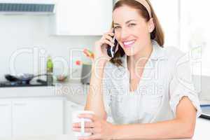 Smiling woman with coffee cup using mobile phone in kitchen