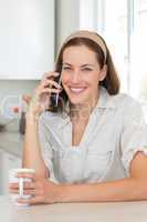 Smiling woman with coffee cup using mobile phone in kitchen