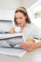 Woman with coffee cup reading newspaper in kitchen