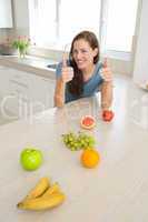 Smiling woman with fruits gesturing thumbs up in kitchen