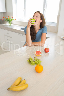 Woman eating apple with fruits on kitchen counter