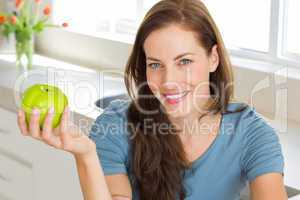 Smiling young woman holding apple in kitchen