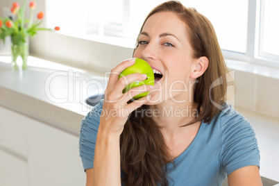 Smiling young woman eating apple in kitchen