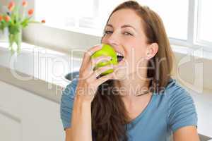 Smiling young woman eating apple in kitchen