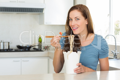 Smiling woman eating noodles in kitchen