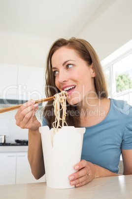Smiling young woman eating noodles in kitchen