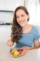 Smiling young woman with fruit salad in kitchen