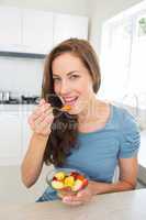 Smiling young woman eating fruit salad in kitchen