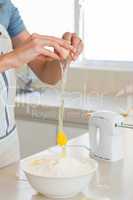 Mid section of woman cracking an egg in bowl at kitchen