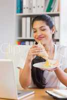 Businesswoman having sandwich while looking at laptop