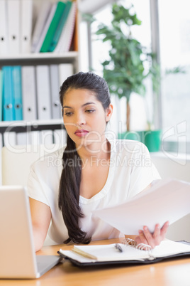 Businesswoman holding documents while using laptop