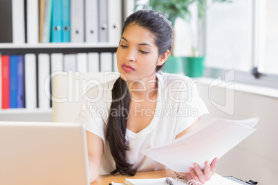 Businesswoman with papers looking at laptop