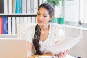 Businesswoman with papers looking at laptop