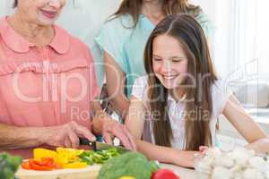 Girl looking at grandmother cutting vegetables