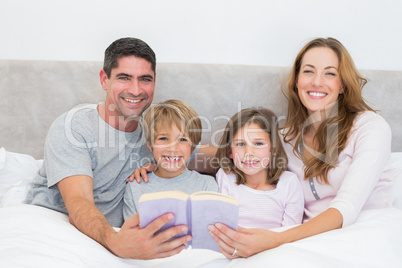 Happy family with storybook in bed