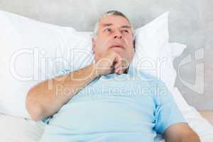 Thoughtful senior man lying in bed