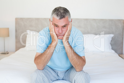 Sad senior man sitting on bed