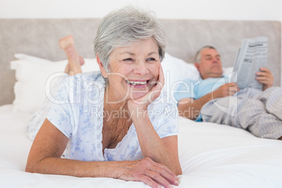 Senior woman with man reading newspaper on bed