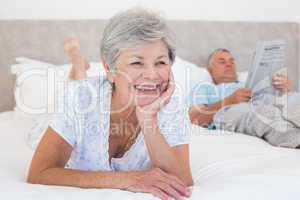 Senior woman with man reading newspaper on bed