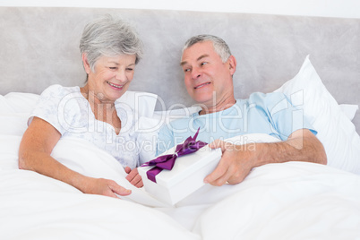 Senior man giving gift box to wife in bed