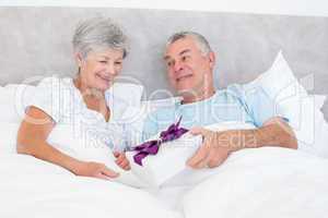 Senior man giving gift box to wife in bed