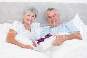 Senior man giving gift to wife in bed