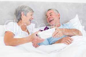 Senior couple holding gift box in bed