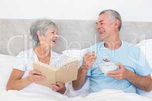 Happy couple with book and bowl in bed
