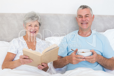 Senior couple with book and bowl in bed