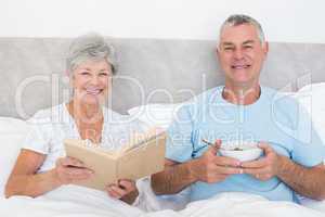 Senior couple with book and bowl in bed