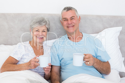 Senior couple holding coffee cups in bed