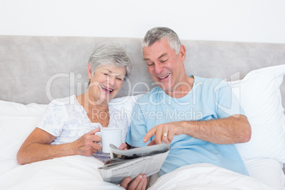 Senior couple reading newspaper in bed