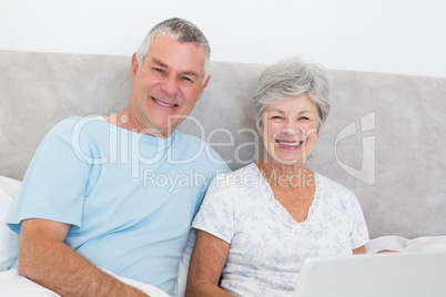 Senior couple with laptop sitting in bed