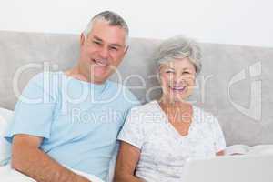 Senior couple with laptop sitting in bed