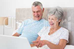 Senior couple laughing while using laptop in bed
