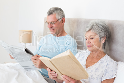 Senior couple reading newspaper and book in bed