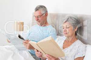 Senior couple reading newspaper and book in bed