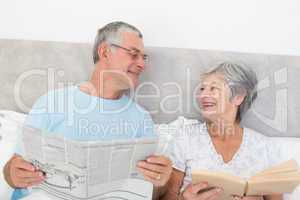 Senior couple with newspaper and book in bed